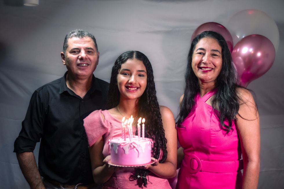 Debutante soprando as velas do bolo ao lado dos pais