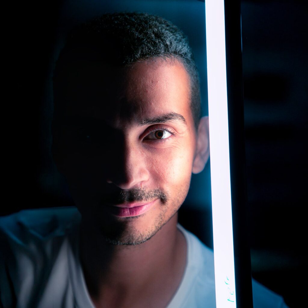 Retrato dramático de um homem com luz de neon vertical ao lado e metade do rosto na sombra.