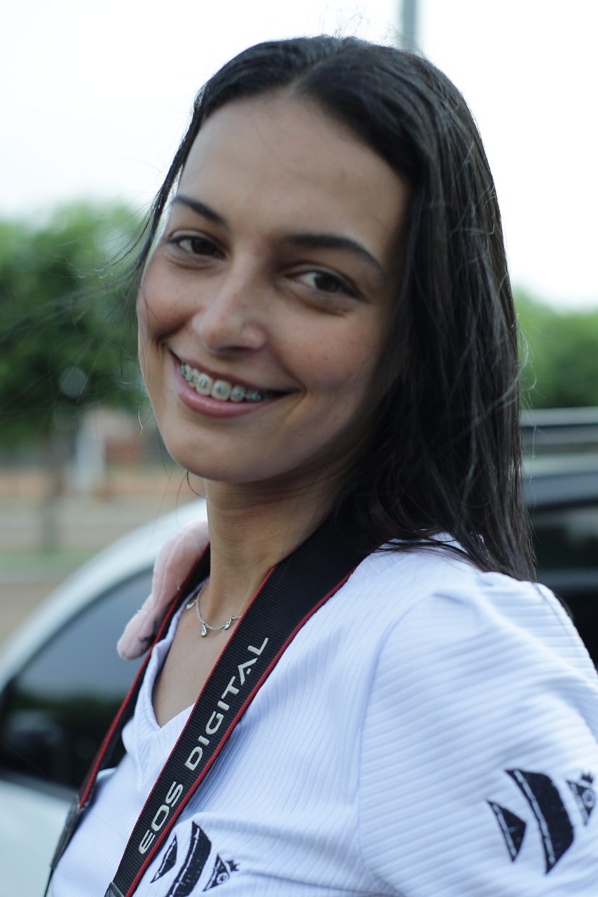 Isa Paiva sorrindo, com a alça da câmera no ombro